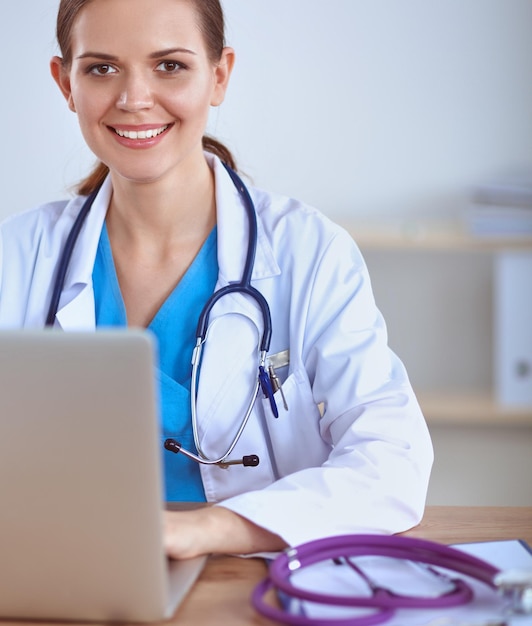 Belle jeune femme médecin souriante assise au bureau et écrivant.