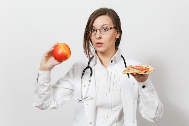 Belle jeune femme médecin avec stéthoscope isolé sur fond blanc. Femme médecin en robe médicale tenant un morceau de pizza à la pomme rouge. Concept de santé du personnel de santé Choix d'une bonne nutrition.