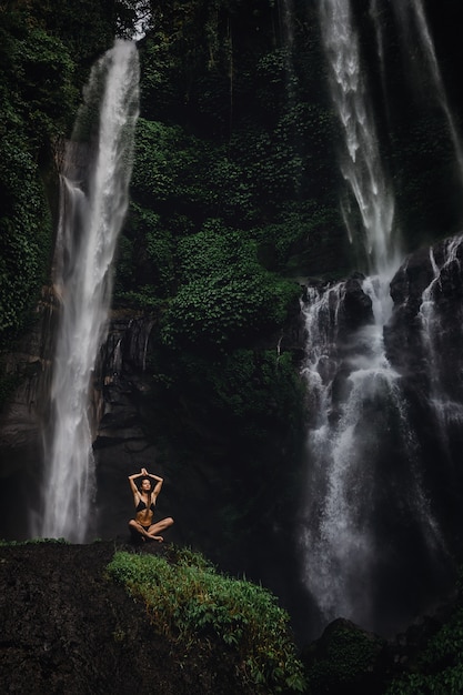 Belle jeune femme méditant en position du lotus tout en faisant du yoga dans une magnifique forêt près de la cascade. Belle femme pratiquant le yoga sur un rocher près de la cascade tropicale