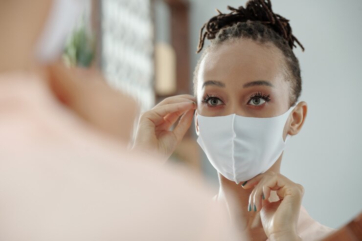 Photo belle jeune femme mettant un masque médical blanc et se regardant dans un miroir