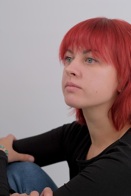 Belle jeune femme mignonne avec une coiffure orange en jeans assis posant en studio sur fond blanc