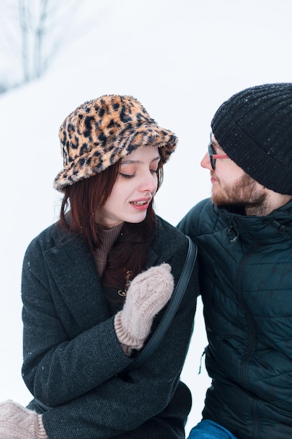 Une belle jeune femme à la mode et un beau gars en vêtements d'hiver à la mode sont assis ensemble dans un parc d'hivers avec de la neige