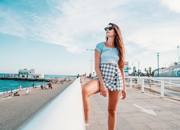 Belle jeune femme à la mode dans des vêtements élégants sexy posant dans la ville moderne avec des gratte-ciel sur fond