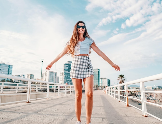 Belle jeune femme à la mode dans des vêtements élégants sexy posant dans la ville moderne avec des gratte-ciel sur fond