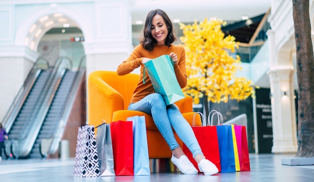 Belle jeune femme à la mode avec de nombreux sacs colorés de bonne humeur avec téléphone intelligent et carte de crédit alors qu'il était assis dans le centre commercial pendant le vendredi noir