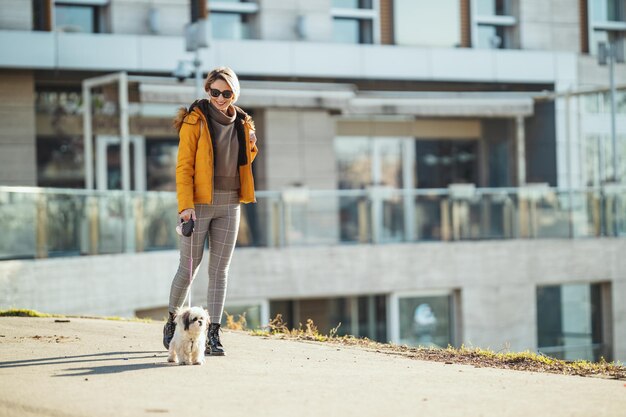 Belle jeune femme de mode passe du temps avec son mignon chien de compagnie, marchant dans la rue de la ville.