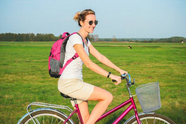 Belle jeune femme monte sur un vélo en été sur le fond des champs verts