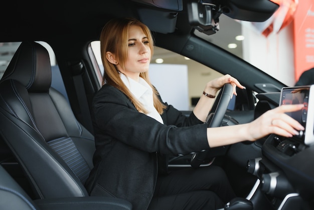 Belle jeune femme montrant son amour pour une voiture dans une salle d'exposition de voiture