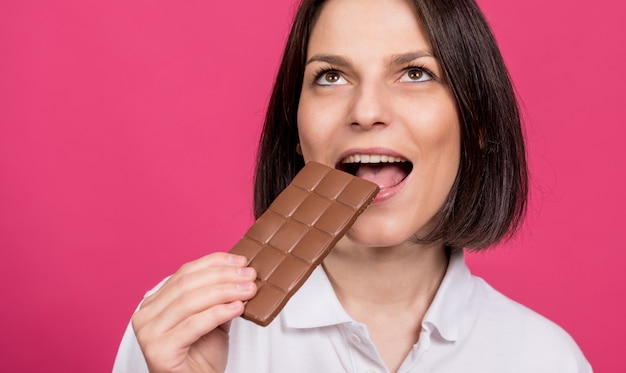 La belle jeune femme mord une barre de chocolat