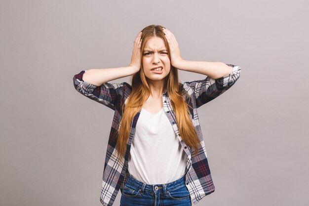 Belle jeune femme sur un mur isolé souffrant de maux de tête désespérés et stressés à cause de la douleur et de la migraine. Mains sur la tête.