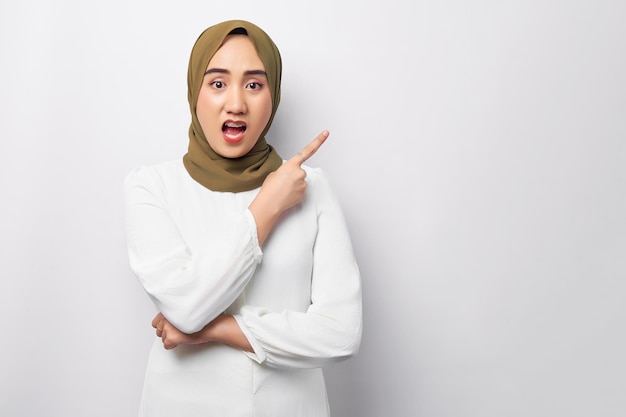 Belle jeune femme musulmane asiatique arabe choquée portant le hijab debout pointant du doigt l'espace de copie vide isolé sur fond blanc Concept de style de vie religieux des gens