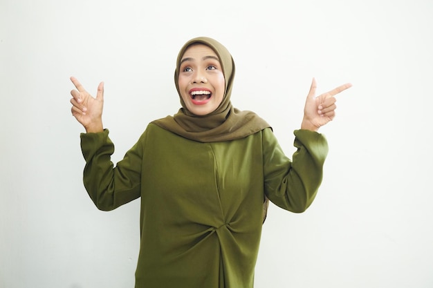 Belle jeune femme musulmane asiatique vêtue d'une robe verte et d'un hijab pointant du doigt l'espace libre