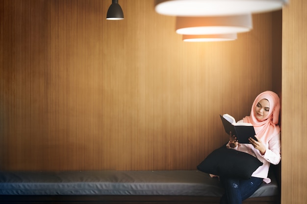 Belle jeune femme musulmane lisant un livre devant un mur en bois avec la surface.