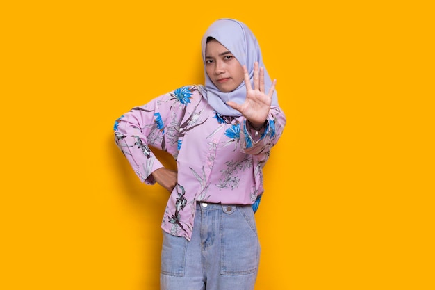belle jeune femme musulmane main faisant un panneau d'arrêt avec une expression sérieuse geste de défense sur jaune