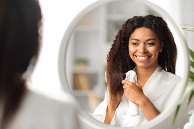 Belle jeune femme noire appliquant un fixatif hydratant sur les extrémités à la maison