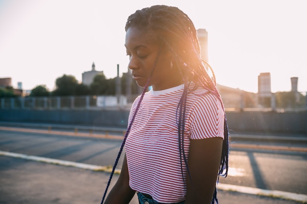 Belle jeune femme noire debout seul rétro-éclairage extérieur songeur