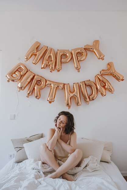 Belle jeune femme en nuisette célébrant le joyeux anniversaire. Surprise du matin en mauvais avec des ballons