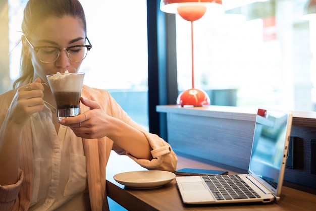 Belle jeune femme avec ordinateur portable, smartphone et café dans un restaurant