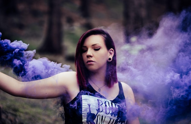 Photo une belle jeune femme par la fumée violette contre les arbres