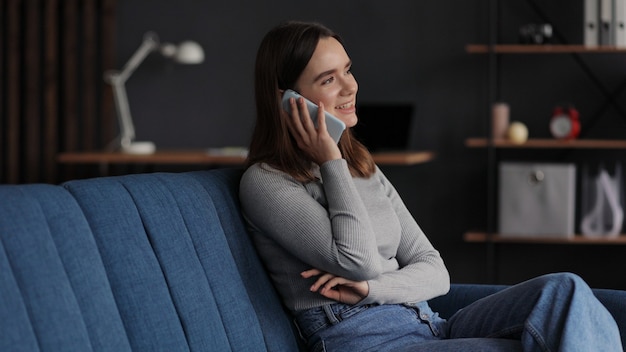 Belle jeune femme parlant au téléphone mobile assis à la maison.