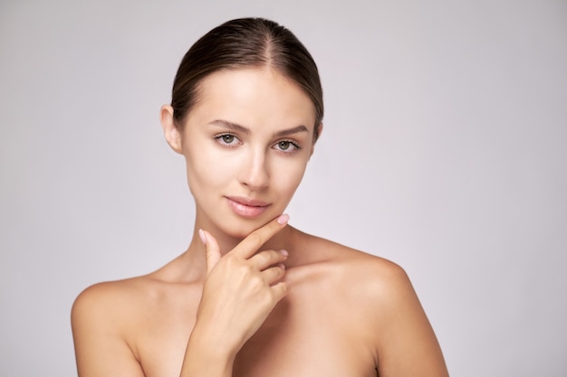 Belle jeune femme avec une peau fraîche et propre debout sur fond gris clair