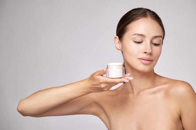 Belle jeune femme avec une peau fraîche et propre debout sur fond gris clair