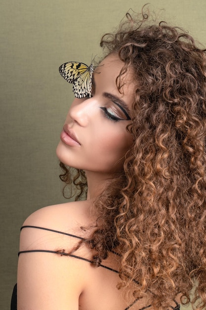 Belle jeune femme avec une peau parfaite et un maquillage jaune vif posant avec un papillon sur son visage