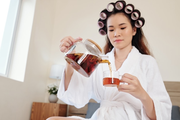 Belle jeune femme en peignoir buvant une tasse de tisane après avoir pris un bain chaud à la maison