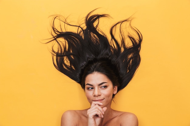 Photo belle jeune femme pensante se trouve isolée sur un mur jaune