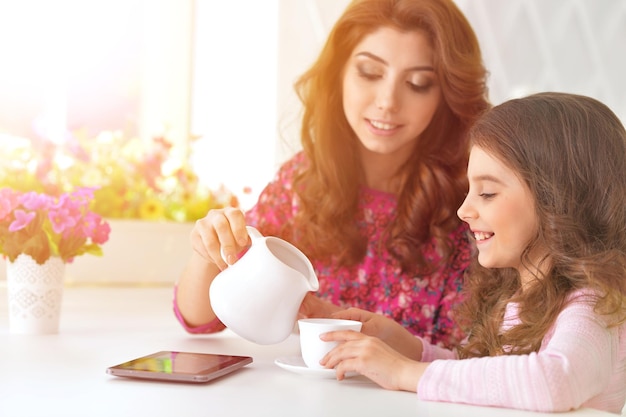 Belle jeune femme et petite fille assise à table. femme versant du lait dans une tasse