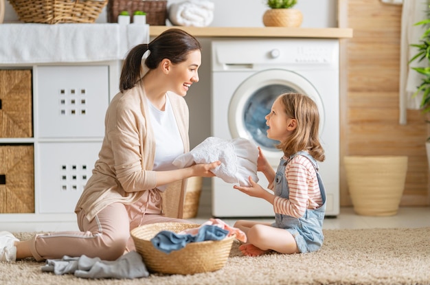 Belle jeune femme et petite fille d'enfant s'amusent et sourient en faisant la lessive à la maison.