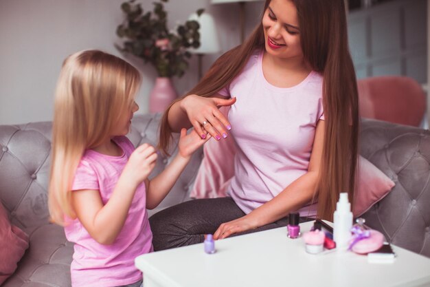 La belle jeune femme et la petite fille regardent leur manucure Maman et sa fille en T-shirts roses sont assises dans la chambre et engagées dans leur beauté