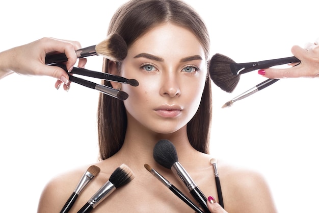 Belle jeune femme avec des pinceaux de maquillage naturels légers pour les cosmétiques et une peau parfaite