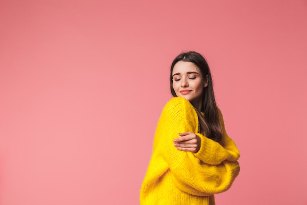 Belle jeune femme portant un chandail chaud debout isolé sur rose, posant