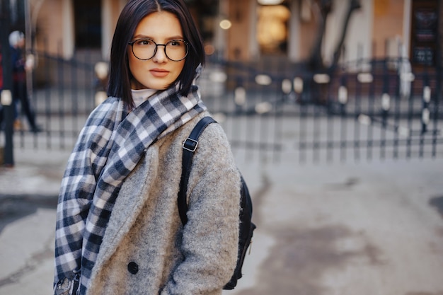 Belle jeune femme portant des lunettes dans un manteau marchant sur une journée ensoleillée