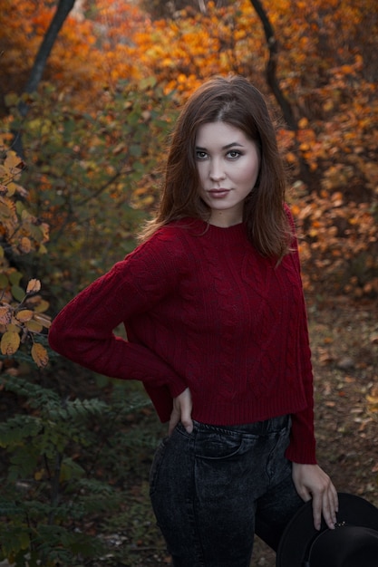 Belle jeune femme portant un pull rouge et un chapeau noir et marchant dans la forêt d'automne. Temps chaud et ensoleillé. Notion d'automne.