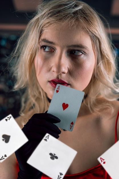 Belle jeune femme portant une robe rouge et un chapeau noir tenant des cartes de poker Aces