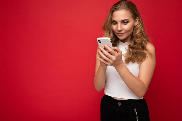 Belle jeune femme portant des vêtements décontractés, isolée sur fond, surfant sur Internet par téléphone en regardant l'écran du mobile.