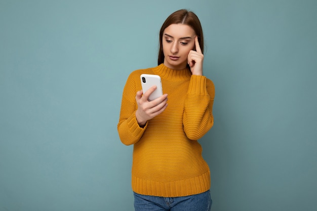 Belle jeune femme portant des vêtements décontractés, isolée sur fond, surfant sur Internet par téléphone en regardant l'écran du mobile.