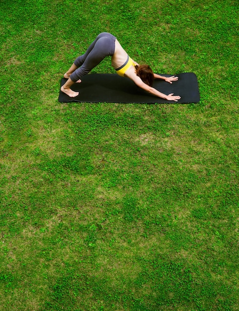 Belle jeune femme portant des vêtements de sport faisant du yoga en plein air le jour d'été