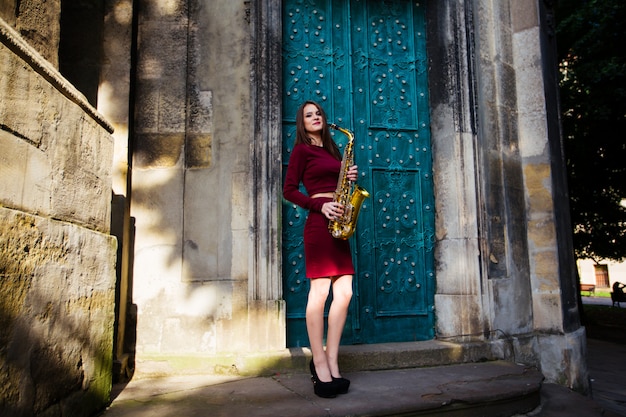 Photo belle jeune femme posant dans les rues de la ville avec son saxophone