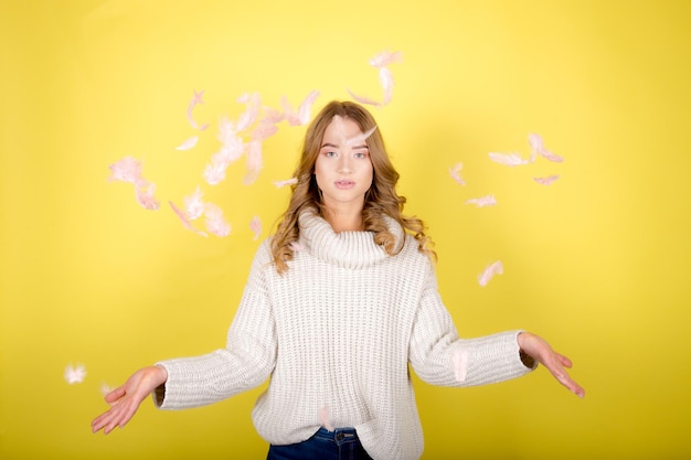 Belle jeune femme posant isolé sur fond de mur jaune avec plume