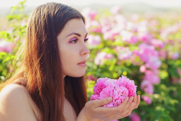 Belle jeune femme posant près de roses dans un jardin.