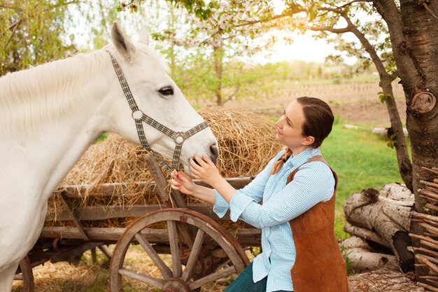 Une belle jeune femme pose à côté d'un cheval blanc