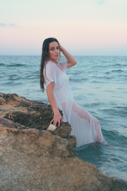 Belle jeune femme pose avec la mer en arrière-plan au coucher du soleil