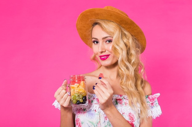 Belle jeune femme avec pot de fruits sur mur rose