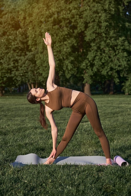Belle jeune femme pratiquant le yoga à l'extérieur dans le parc assis sur un tapis