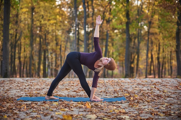 Photo belle jeune femme pratique le yoga asana triangle pose trikonasana sur la terrasse en bois dans le parc en automne