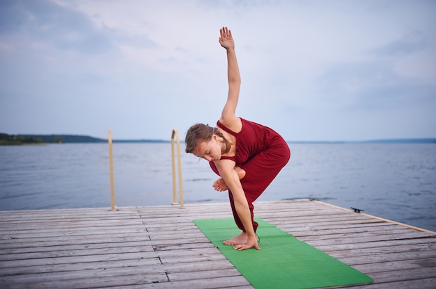 Belle jeune femme pratique le yoga sur la terrasse en bois près du lac