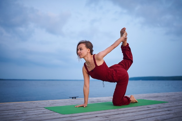 Belle jeune femme pratique le yoga sur la terrasse en bois près du lac